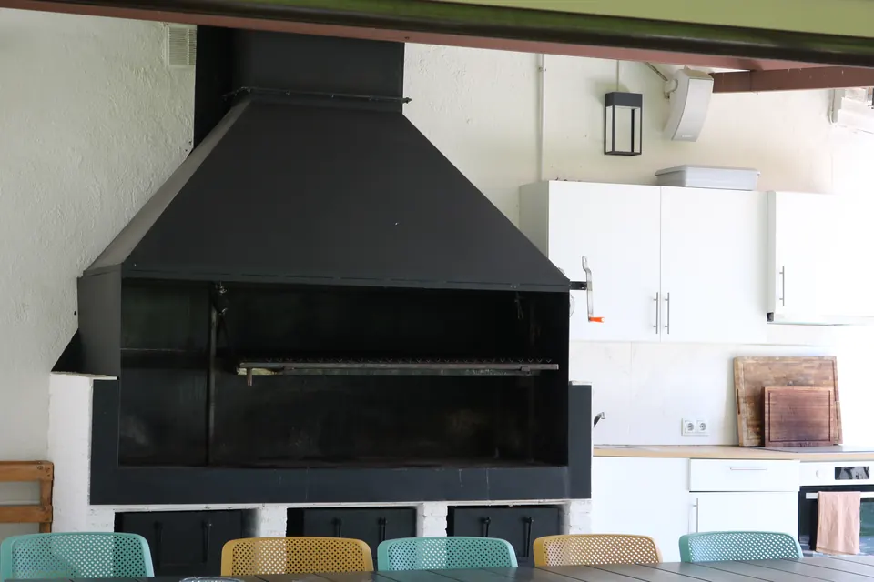 La gran campana negra de la barbacoa junto a la cocina exterior, con la mesa larga delante