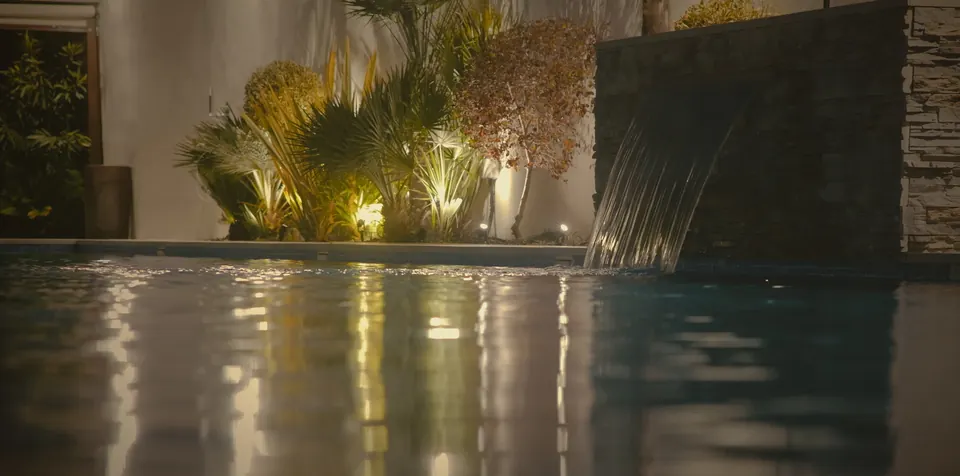 Lámina de agua cayendo sobre la piscina, iluminada de noche