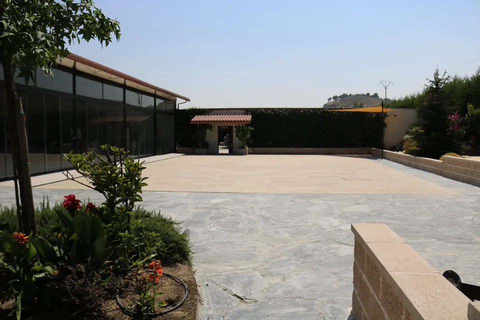 La explanada de travertino con los macizos de flores en primer plano y el hangar a un lado