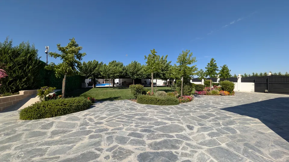 El empedrado del jardín que baja hacia la piscina, entre setos y arbolado joven