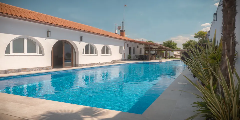 Piscina de la finca con la fachada encalada al fondo, en Seseña