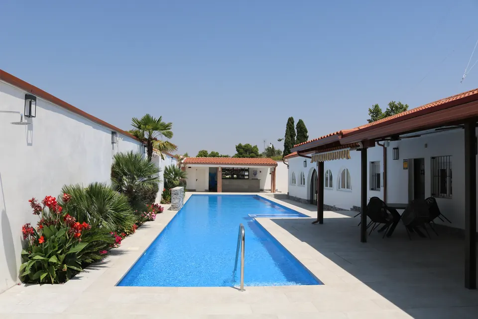 La piscina con los macizos de flores rojas en primer plano y el porche al fondo